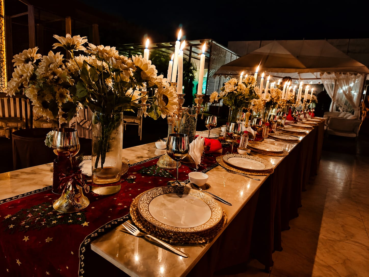 Candlelit rooftop dinner set for two on a carved sandstone terrace in Jaipur, with rose petals, silver tableware, and the city's skyline at dusk