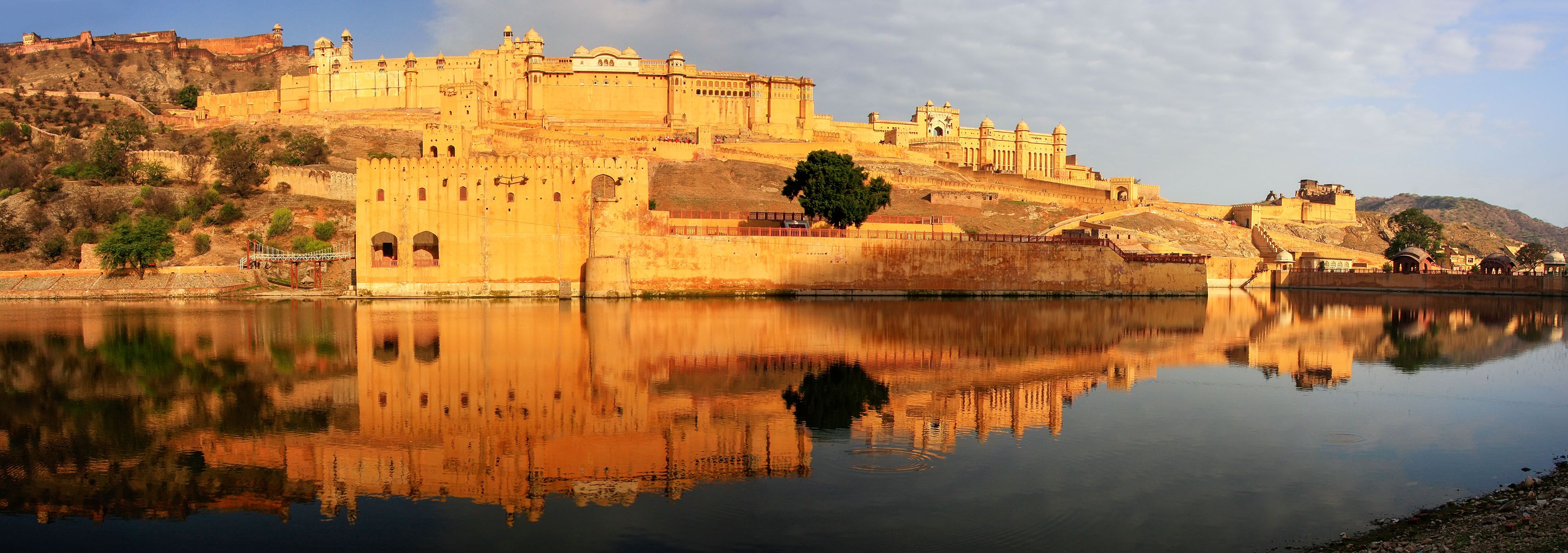 Amber Fort rising above Maota Lake in the golden light of early morning, reflected in still water, viewed from the approach road in Jaipur