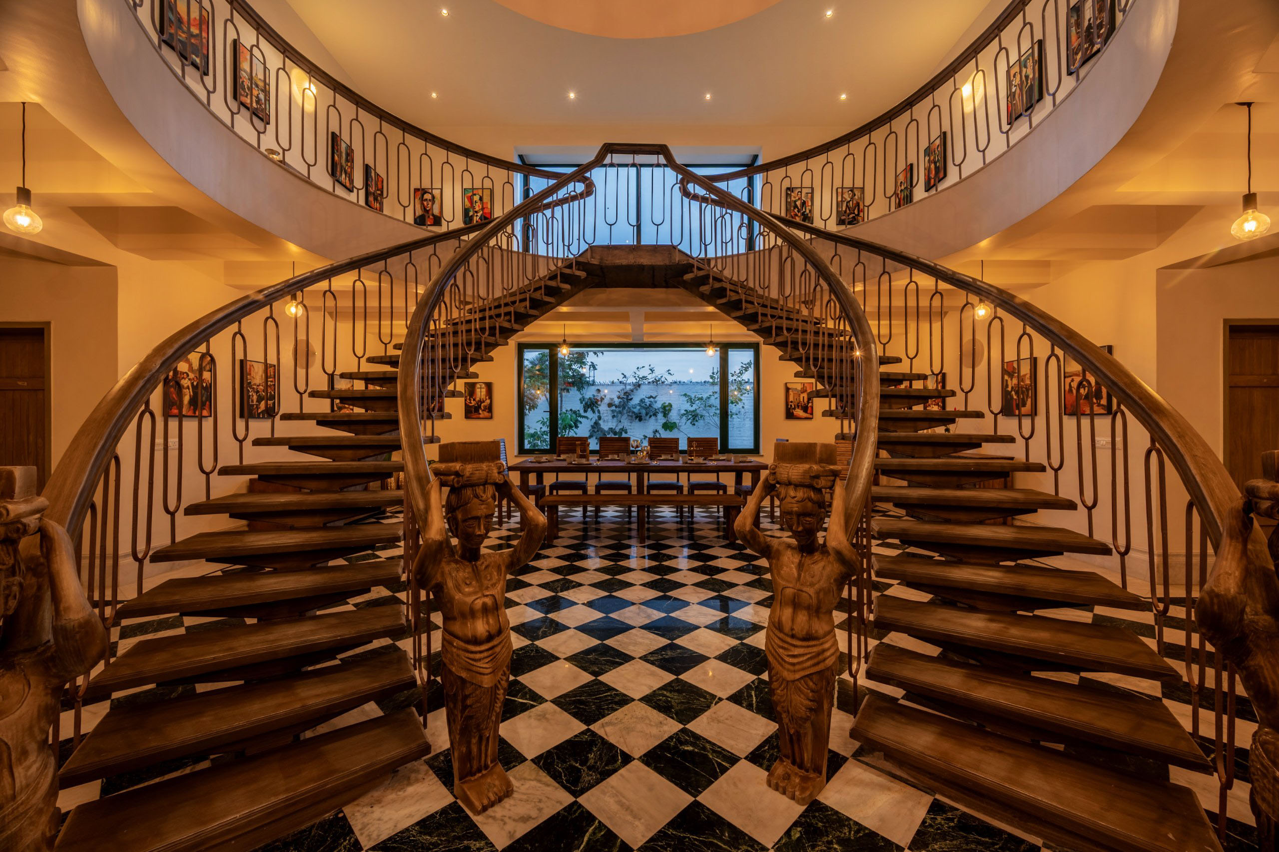 Large spiral staircase in a mansion leading to a dining room with a table and chairs