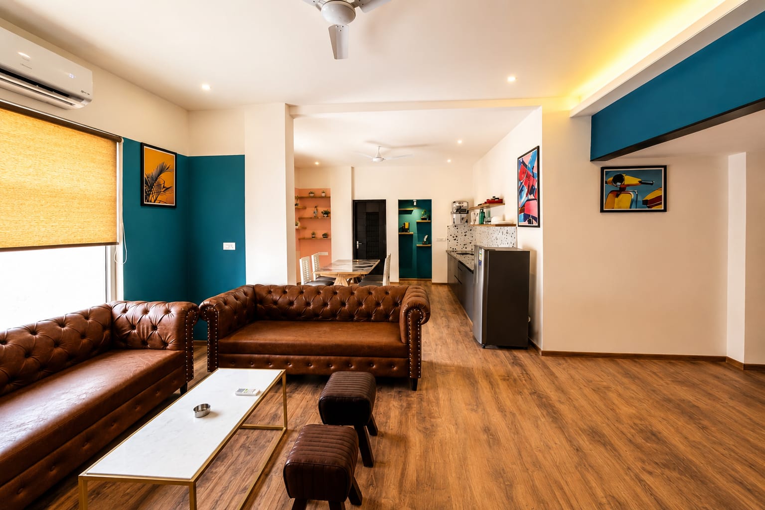 A large living room with a brown couch, a coffee table, and a chair, with a dining table and potted plant